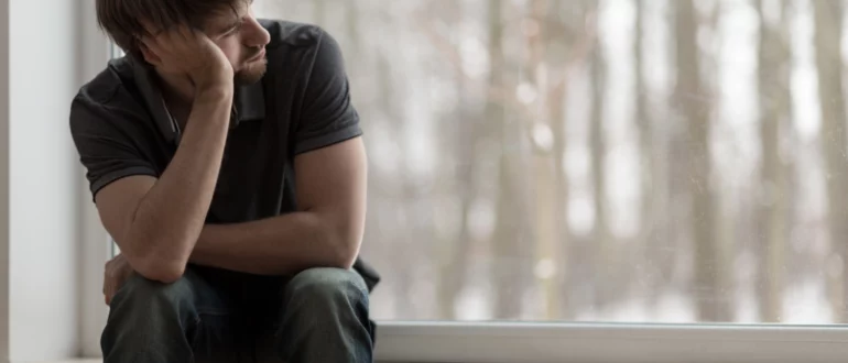 Ein Mann mit passiven Selbstmordgedanken sitzt auf einer Fensterbank, stützt sich auf seinen Arm und schaut nach draußen.