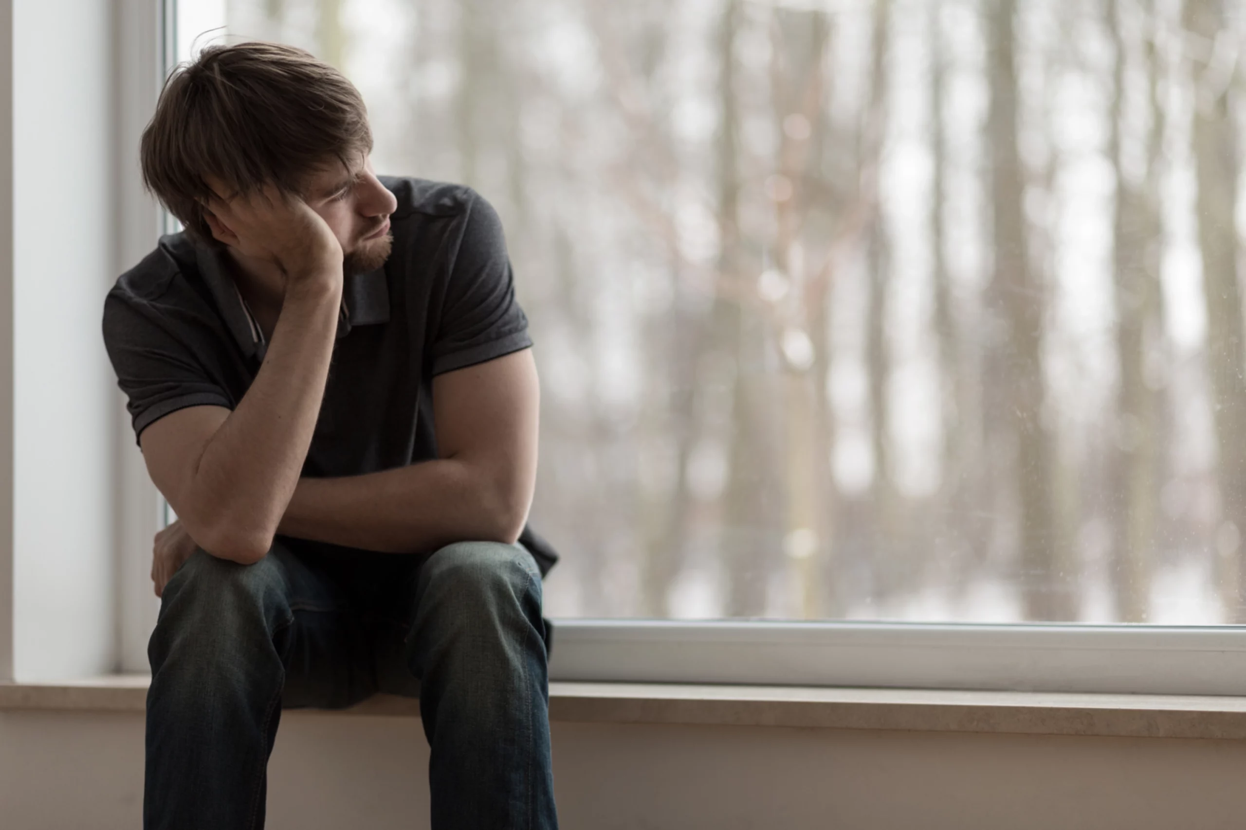 Un uomo con pensieri passivi di suicidio si siede sul davanzale di una finestra, si appoggia al braccio e guarda fuori.